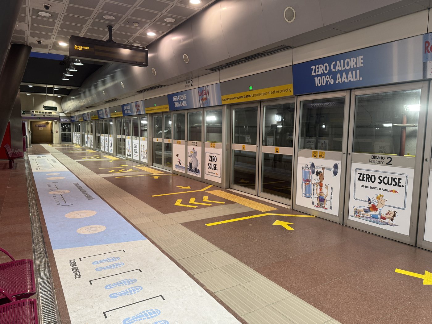 Banchina della stazione M5 San Siro Stadio con allestimento Red Bull Zero Scuse — porte vetrate, cartelli Zero Calorie 100% Aaali, indicazioni a pavimento